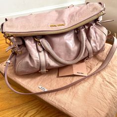 Authentic Miu Miu Vitello Lux Large Bow Bag In Mughetto. A Beautiful And Sophisticated Shade Of Dusky Pink. Minimal Use Has Preserved The Bag In Gently Loved Vintage Condition. Some Light Discoloration On Exterior That Comes From The Natural Aging Of Premium Leather And Hardware As Shown In Photos. Interior Is Pristine. Can Likely Be Serviced At Any Leather Goods Shop To Be Brought To Premium Condition. The Bag Features Rolled Leather Top Handles With An Optional Shoulder Strap, Leather Straps And Brass Links, Decorative Side Leather Bows And A Top Zipper And Zipper Pull. This Opens To A Deep Purple Interior With A Zippered Pocket Branded With Miu Miu Logo Hardware. Approx Measurements: High-end Pink Bag With Handles, High-end Pink Satchel, High-end Pink Satchel With Detachable Handle, High-end Pink Bag With Dust Bag Included, High-end Pink Top Handle Satchel, High-end Pink Leather Shoulder Bag, Designer Pink Bag With Dust Bag, Designer Pink Bags With Dust Bag, Miu Miu Shoulder Bag With Top Carry Handle