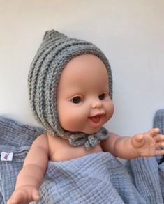 a baby doll wearing a knitted hat and blue blanket on top of a bed