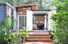 a small house made out of shipping containers in the middle of some trees and plants