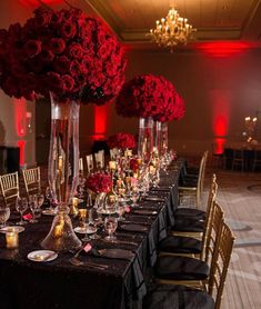 a long table is set up with black linens and red roses in tall vases