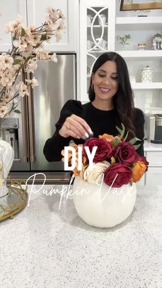 a woman standing in front of a white counter top with flowers on it and the words diy pumpkin vase