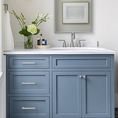 a bathroom with blue cabinets and white counter tops, flowers in vase on the sink