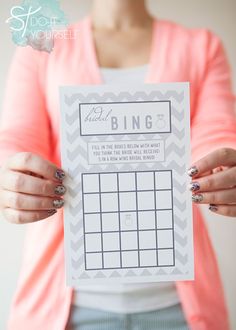 a woman holding up a printable photo to show off her bridal bingo game