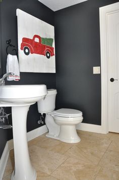 a white toilet sitting next to a sink in a bathroom under a painting on the wall