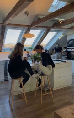 two people sitting on stools in front of a kitchen counter with an open window