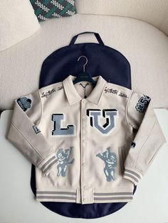 Embrace a playful take on iconic luxury with the Louis Vuitton-inspired Varsity Jacket. This statement piece showcases a luxurious cream-colored body complemented by smooth leather sleeves, capturing the essence of classic varsity style. The jacket is adorned with meticulously embroidered patches, showcasing the iconic "LV" initials, playful mascot motifs, and signature Louis Vuitton text, adding a touch of whimsical sophistication. The ribbed collar, cuffs, and hem ensure a snug and comfortable Luxury Varsity Jacket For College In Fall, Luxury Varsity Jacket For Fall Streetwear, Luxury Fall Varsity Jacket For Streetwear, Luxury Fall Varsity Jacket For College, Luxury Long Sleeve Varsity Jacket For College, Luxury White Outerwear For Streetwear, Luxury White Streetwear Outerwear, Luxury Long Sleeve Varsity Jacket, Louis Vuitton Varsity Jacket