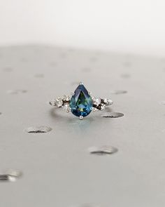 a blue diamond ring sitting on top of a silver surface with drops of water around it