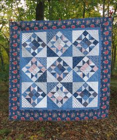 a blue and white quilt hanging from the side of a tree in front of some leaves