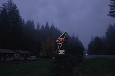 a motel sign lit up at night in the foggy forest with cars parked nearby