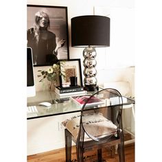 a glass desk with a lamp and pictures on the wall behind it in a home office