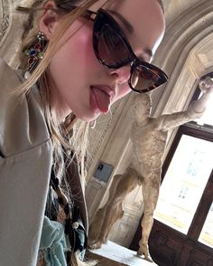 a woman wearing sunglasses standing in front of a statue