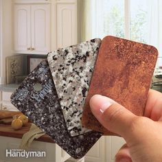 a hand holding four coasters in front of a kitchen counter top with white cabinets