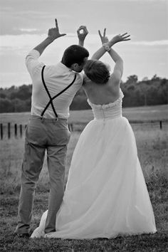 a man and woman standing next to each other in front of a field with their hands up