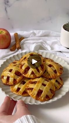 a person holding a white plate with some pies on it and an apple in the background