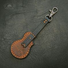 a guitar keychain is shown on a black leather surface with a stitching pattern