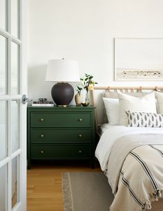 a bedroom with white walls and green dresser next to the bed in front of it