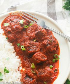 a white plate topped with rice and meat covered in red sauce next to a fork