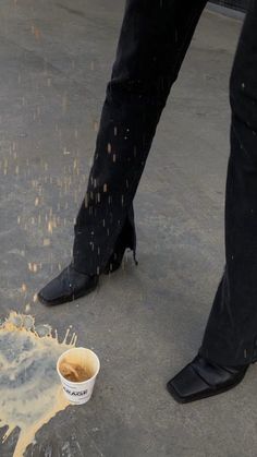 a person standing next to a cup of coffee on top of a cement ground covered in yellow liquid