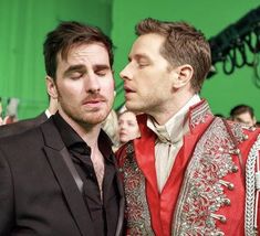 two men dressed in red and black standing next to each other at a fashion show