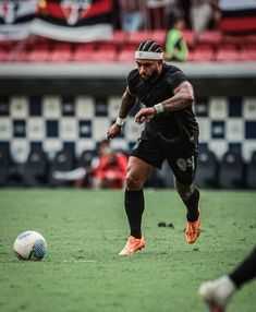 a man in black uniform kicking a soccer ball on field with people watching from the bleachers