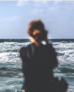 a blurry photo of a person standing in front of the ocean with their hand on his ear