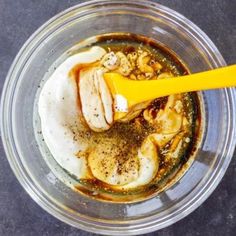 a glass bowl filled with food on top of a black counter next to a yellow spoon