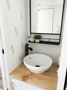 a white sink sitting on top of a wooden counter next to a mirror and black faucet