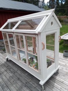 a small white greenhouse sitting on top of a wooden deck