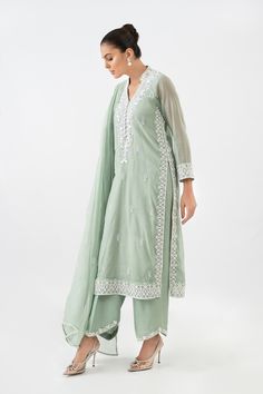 Introducing a charming ensemble featuring a basil green cotton net shirt, delicately hand embroidered and adorned with resham and French knot work. The intricate detailing adds a touch of elegance to the overall design. The shirt is paired with loose-fitting pants in a matching shade, featuring similar resham work on the bottoms, creating a cohesive look. To complete the ensemble, a handworked chiffon dupatta with lace edging is included, providing a graceful finishing touch. Lily Of The Nile, Net Shirt, Resham Work, Loose Fitting Pants, Fitting Pants, The Nile, Chiffon Dupatta, French Knot, Lace Edging