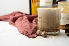 a glass filled with liquid sitting on top of a counter next to bottles and a towel