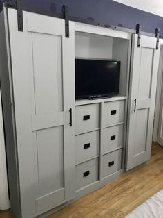 an entertainment center with sliding doors and drawers in a room that has hardwood floors, blue walls and white cabinets