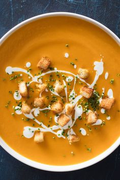 a white bowl filled with soup and croutons on top of a blue table