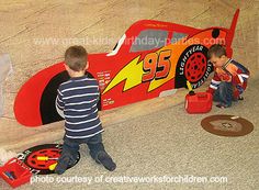 two young boys playing in front of a red race car on the floor with other children