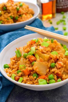 two bowls filled with rice and vegetables next to chopsticks on a blue towel