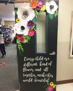 a door decorated with paper flowers and writing on the front, says every child is a different kind of flower, and all together makes world beautiful