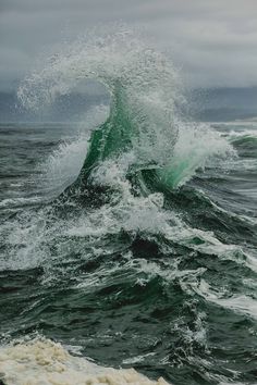 an ocean wave hitting the top of a green and white surfboard in rough waves