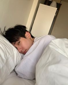 a young man laying in bed with white sheets