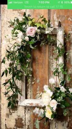 a white frame with flowers and greenery hanging from it's side on a wooden wall