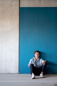 a young man sitting on the ground in front of a blue wall