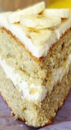 a slice of banana cake with white frosting and sliced bananas on top, sitting on a plate