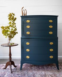 a dark blue dresser with gold handles and knobs on the drawers next to a small table