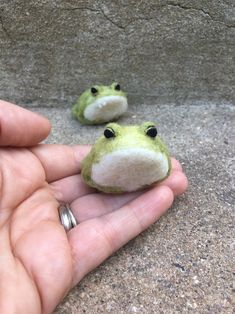 someone is holding two small stuffed animals in their hand, one green and the other white