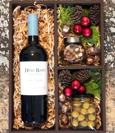 a bottle of wine in a wooden box filled with nuts and other holiday decorations next to a candle