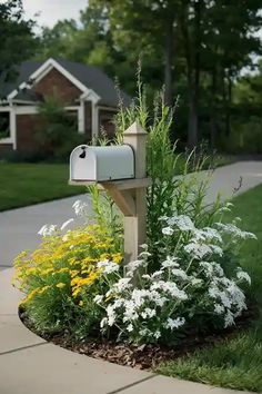 a mailbox sitting in the middle of a flower bed next to a sidewalk and trees