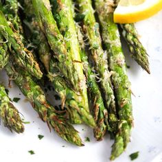 asparagus with parmesan cheese and lemon wedges on a white plate