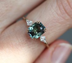 a woman's hand holding an engagement ring with a green and white diamond