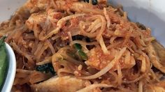 a white bowl filled with noodles and meat next to a green pepper on the side