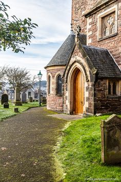 an old stone church with a wooden door and graves in the grass next to it