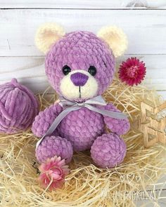 a purple teddy bear sitting on top of hay next to a pink ball of yarn