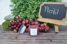 a candle sits next to grapes and a chalkboard sign that says merlot on it